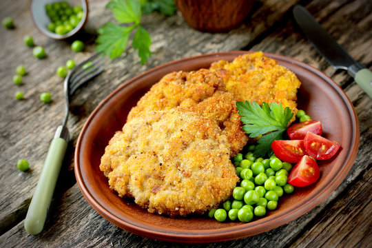 Pork cutlet in bread crumbs with tomato and green peas on a wood