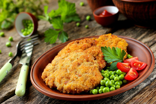 Pork cutlet in bread crumbs with tomatoes and green peas