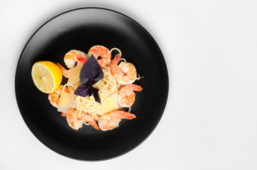 Spaghetti with grilled shrimps on a black plate with lemon and basil