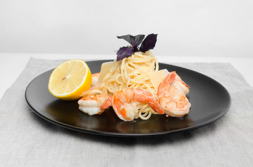 Spaghetti with grilled shrimps on a black plate with lemon and basil