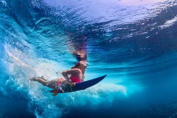 Foto op Plexiglas Jong actief meisje in bikini in actie - surfer met surfplank duik onder water onder grote oceaangolf. Gezinslevensstijl, watersportavonturenkamp voor mensen en extreem zwemmen op het strand tijdens de zomervakantie. © Tropical studio