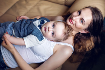 Obraz na płótnie Canvas happy mother in white tank top laying with my son on a light sofa