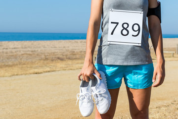 Athlete with race start number holding running shoes.