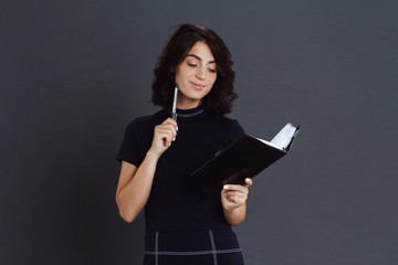 Beautiful thoughtful young woman posing over grey background and holding notebook in hands
