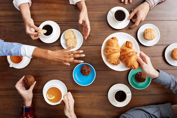 Picture of people's hands on wooden table with croissants and coffee. 
