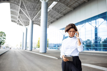 Fototapeta premium Young successful businesswoman speaking on phone, standing near business centre.