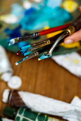 Close up of hands holding brushes and palette knife.