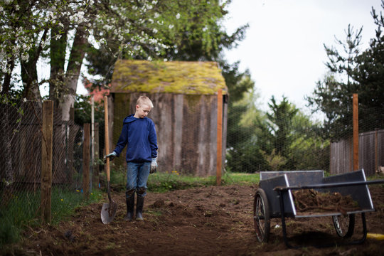 Young boy standing in a garden holding a shovel