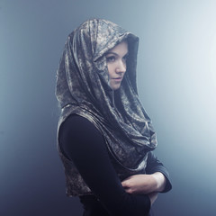 Young beautiful woman in stylish Cape with hood. Portrait on dark background, smoke and fog