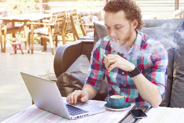 Stylish vapor sitting in cafe. Modern handsome man with laptop outdoor