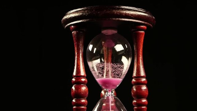 Sand goes through the hole of the clock. Black. Slow motion. Close up