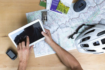 Desk with hands on a map, tablet pc and bike accessoires, elevated view
