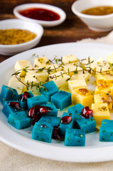 Cheese platter, Gouda, feta, blue pesto cheeses on white plate with herbs, olive oil, pomegranate and mustard sauces