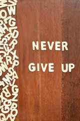Word never give up made with block wooden letters next to a pile of other letters over the wooden board surface composition