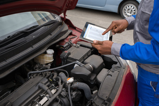Mechanic With Digital Tablet While Examining Car