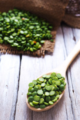 Close up of a spoon of peeled split green pea on a wooden table.