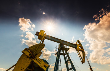 Oil field with old pump jack, profiled on blue sky with white clouds, on a bright day