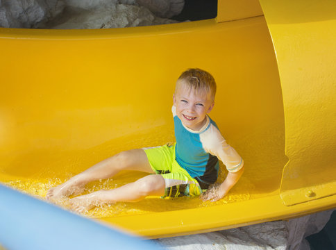 Smiling Young boy riding down a yellow water slide at an outdoor waterpark