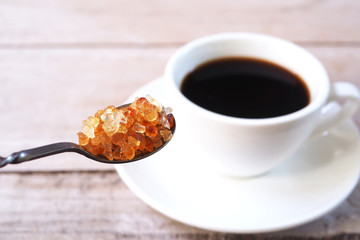 Close up of caramel sugar in a spoon with black coffee on a wooden table. Selective focus