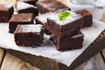 Chocolate brownies with powdered sugar and cherries on a dark wooden background. Selective focus.