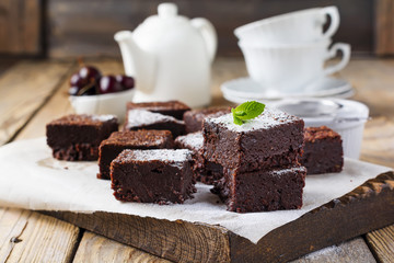 Chocolate brownies with powdered sugar and cherries on a dark wooden background. Selective focus.
