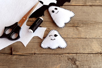 Halloween funny white ghosts diy, felt sheets, scissors, thread, needles on an old wood background. Easy Halloween felt bringing ornament. Sewing crafts idea for children