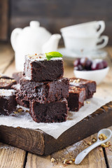 Chocolate brownies with powdered sugar and cherries on a dark wooden background. Selective focus.