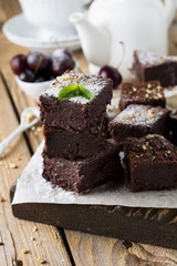 Chocolate brownies with powdered sugar and cherries on a dark wooden background. Selective focus.