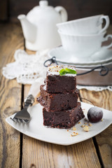 Chocolate brownies with powdered sugar and cherries on a dark wooden background. Selective focus.