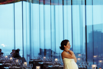 Pregnant bride holds her nack daydreaming in an empty cafe