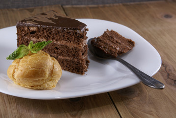 Dessert on a plate on a rustic wooden table: profiterole, decorated with mint leaves and a slice of chocolate cake