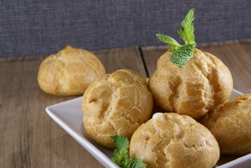 Cakes profiteroles decorated with mint leaves lying on a rustic wooden table