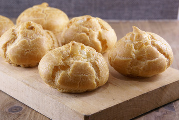 Cakes profiteroles decorated with mint leaves lie on a chopping board, which lies on a rustic wooden table