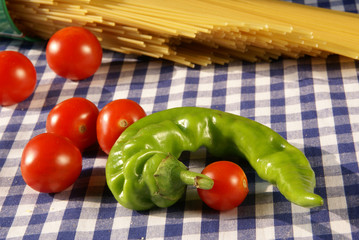 Ingredients for cooking pasta: spaghetti, tomato and pepper lying on a checkered tablecloth on the table.