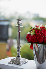 metal high-quality silver candlestick on a green background, with red roses