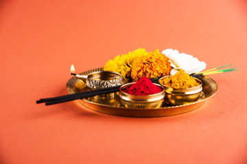 Fototapeta premium Beautifully Decorated Pooja Thali for diwali celebration to worship, huldi or turmeric powder and kumkum, flowers, scented sticks in brass plate on orange background, hindu puja thali