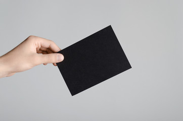 Black A6 Flyer / Postcard / Invitation Mock-Up - Male hands holding a black flyer on a gray background.