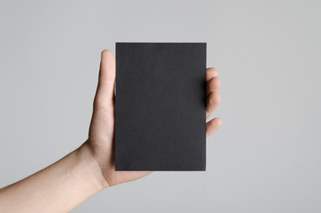 Black A6 Flyer / Postcard / Invitation Mock-Up - Male hands holding a black flyer on a gray background.
