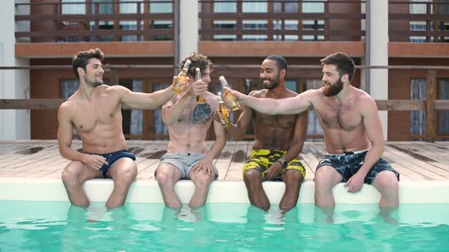 Handsome young smiling men having fun in swimming pool and drinking beer