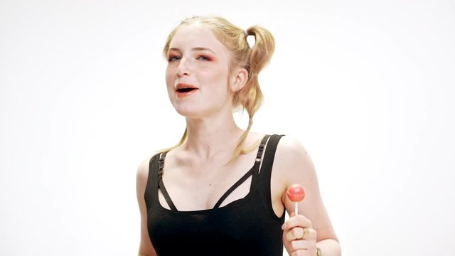 Young beautiful girl dancing, smiling, holding chupa chups over white background. Slow motion.