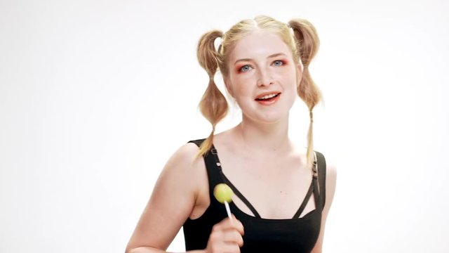 Young beautiful girl dancing, smiling, holding chupa chups over white background. Slow motion.