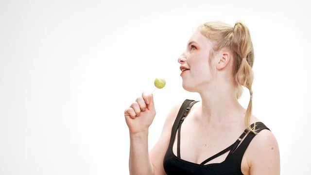 Young beautiful girl dancing, smiling, holding chupa chups, singing over white background. Slow motion.
