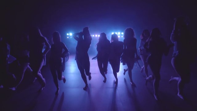 Shilouettes of female dancers group sensually walking on a dark stage with lights and smoke - 4k video