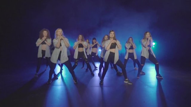 Dance performance of pretty female group on a dark stage with blue lights and smoke