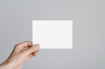 A6 Flyer / Postcard / Invitation Mock-Up - Male hands holding a blank flyer on a gray background.
