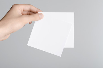 Square Flyer / Invitation Mock-Up - Male hands holding blank flyers on a gray background.