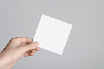 Square Flyer / Invitation Mock-Up - Male hands holding a blank flyer on a gray background.