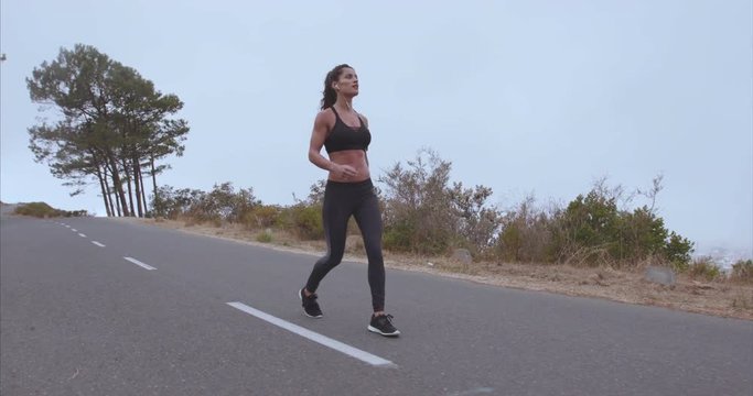 Fitness woman walking on country road. Young woman in sportswear taking morning walk on countryside highway.
