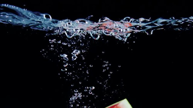 Fresh ripe watermelon slice falls into water with splashes on black background