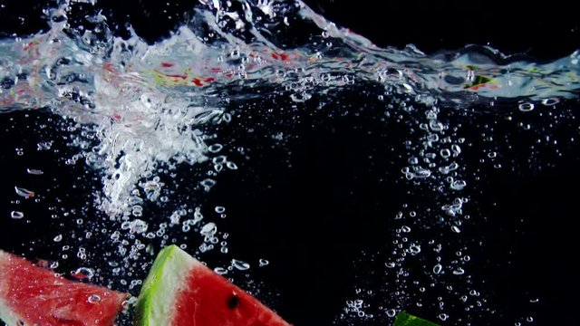 Fresh ripe watermelon slices falls into water with splashes on black background slow motion close-up